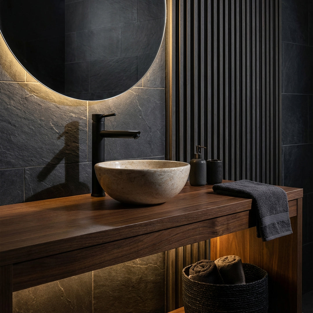 Ronde opzetwastafel van licht natuursteen op een donkerhouten wastafel met zwart beslag in een elegante badkamersfeer