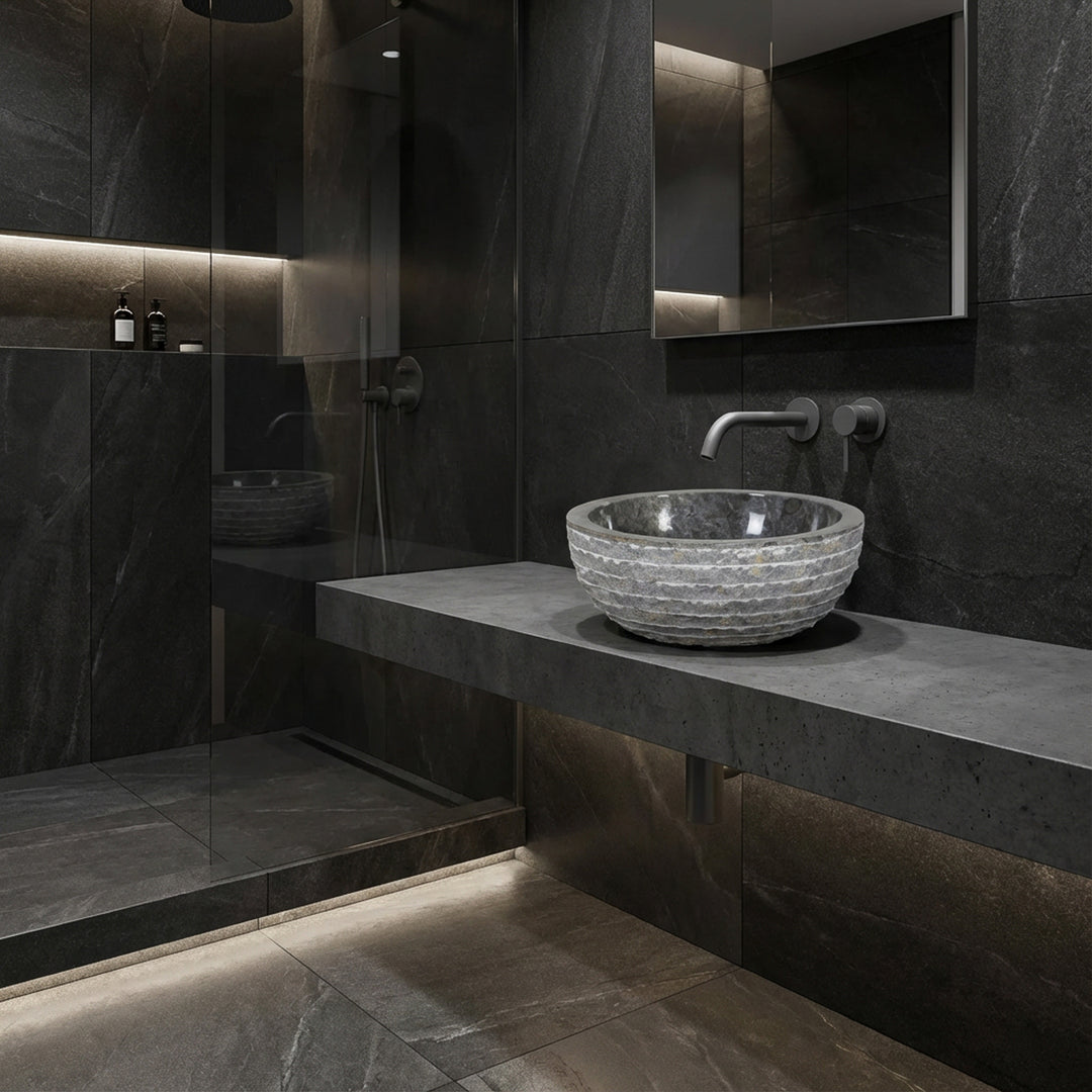 Ronde stenen aanrechtwastafel op zwevende console, moderne badkamer met donkere tegels, glazen douche en indirect licht