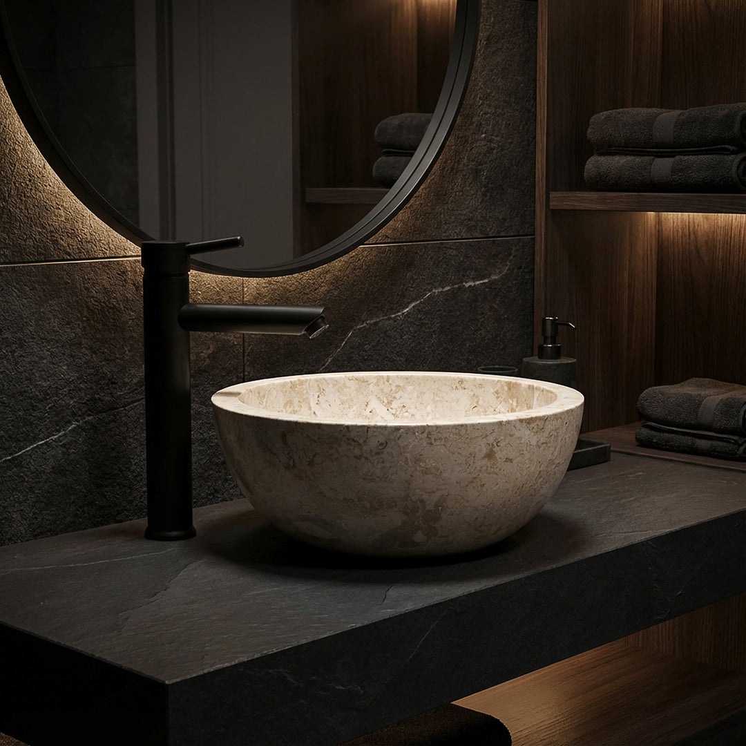 Ronde opzetwastafel van licht marmer op een donkere stenen plaat met zwart armatuur in een elegante badkamersfeer