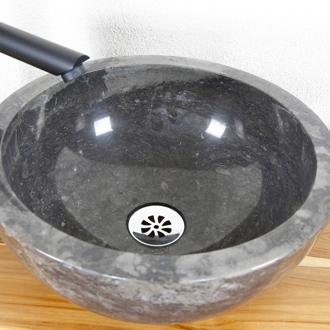 Detailansicht eines runden Aufsatzbeckens aus Stein mit polierter Innenfläche und mittigem Ablauf auf Holzplatte