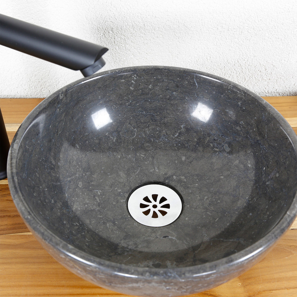 Ronde opzetwastafel van natuursteen in detail met gepolijst binnenoppervlak, RVS afvoer en armatuur