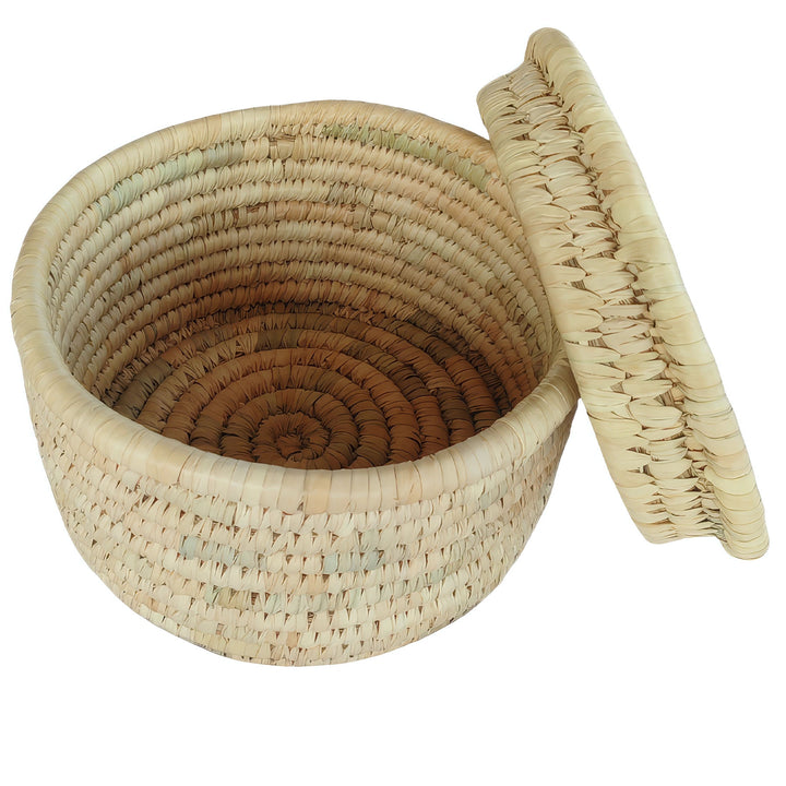 Ronde gevlochten mand van palmbladeren met een diameter van 28 cm, een aan de zijkant aangebrachte deksel en een zichtbare binnenruimte.