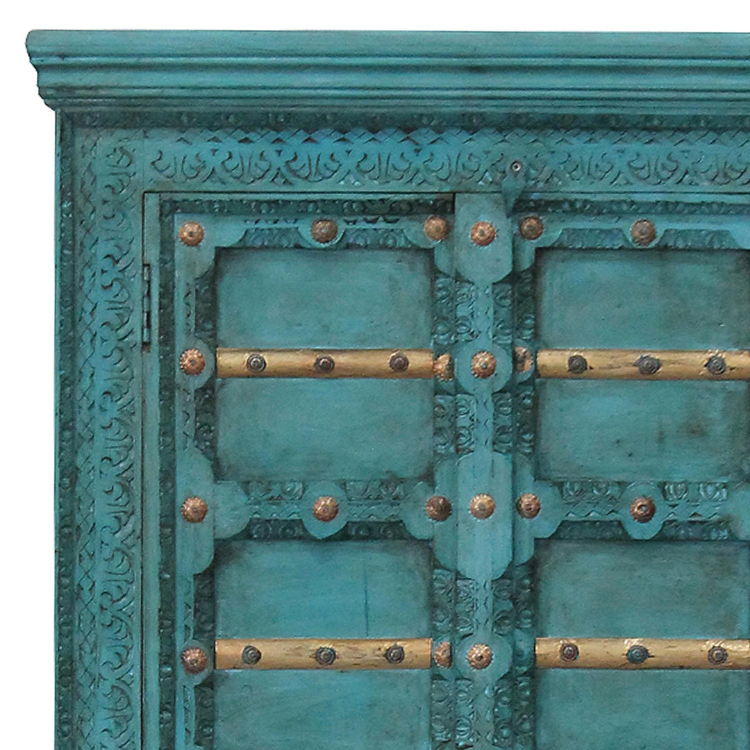 Detail van de turquoise ornamenten op de kastdeuren, met goudkleurige dwarslijsten en decoratief beslag.