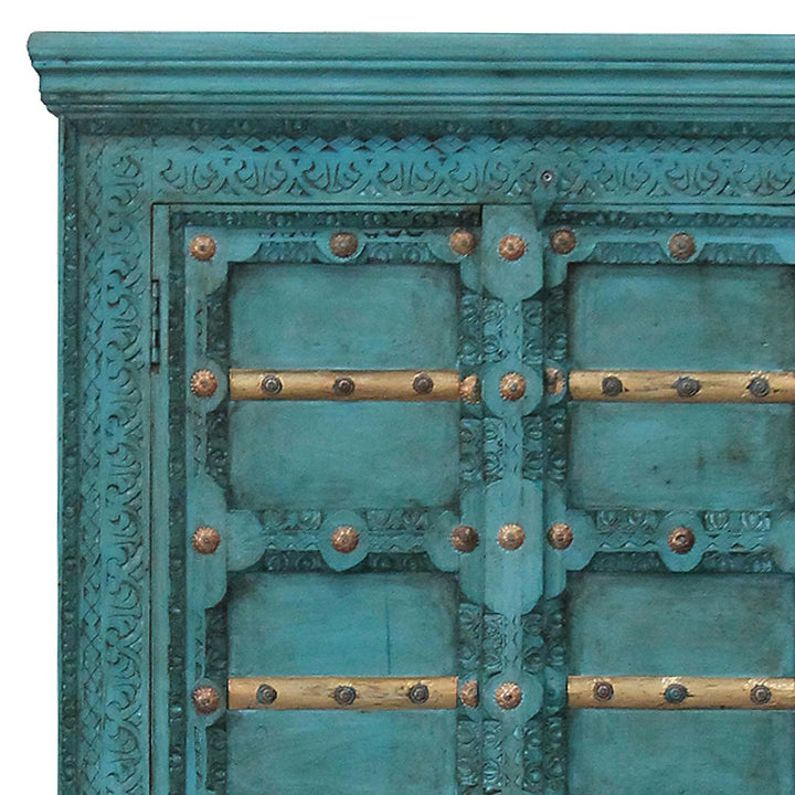Detail van de turquoise ornamenten op de kastdeuren, met goudkleurige dwarslijsten en decoratief beslag.