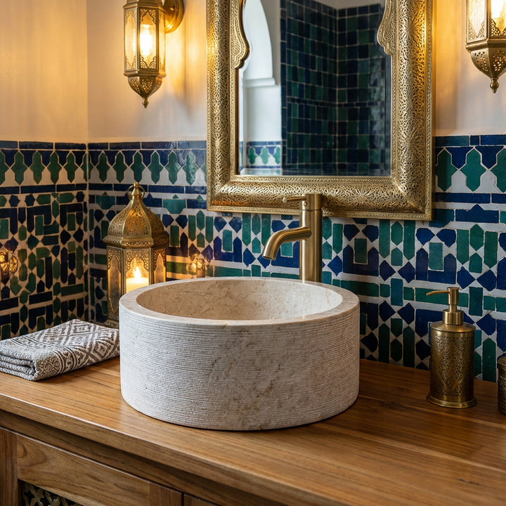 Rond marmerWastafel op een houten console, sfeervol geënsceneerd in de oosterse badkamer met mozaïektegels en messing details.