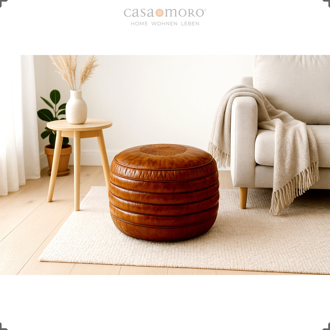 Helles Wohnzimmer im skandinavischen Stil mit rundem Leder Pouf in Braun auf Teppich, beigem Sofa und Holzhocker mit Vase – ruhiges, natürliches Ambiente.