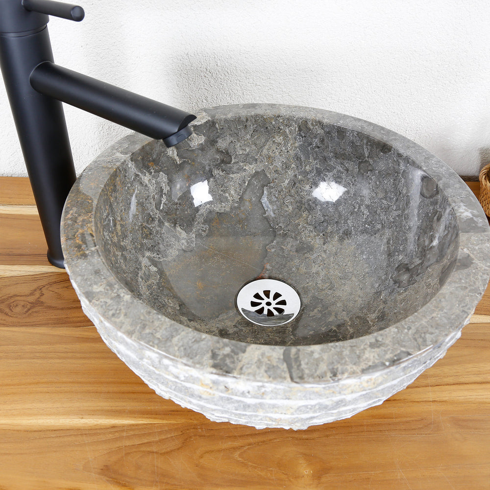 Ronde opzetwastafel van natuursteen met een gepolijste binnenkant en een gestructureerde buitenrand op een houten blad