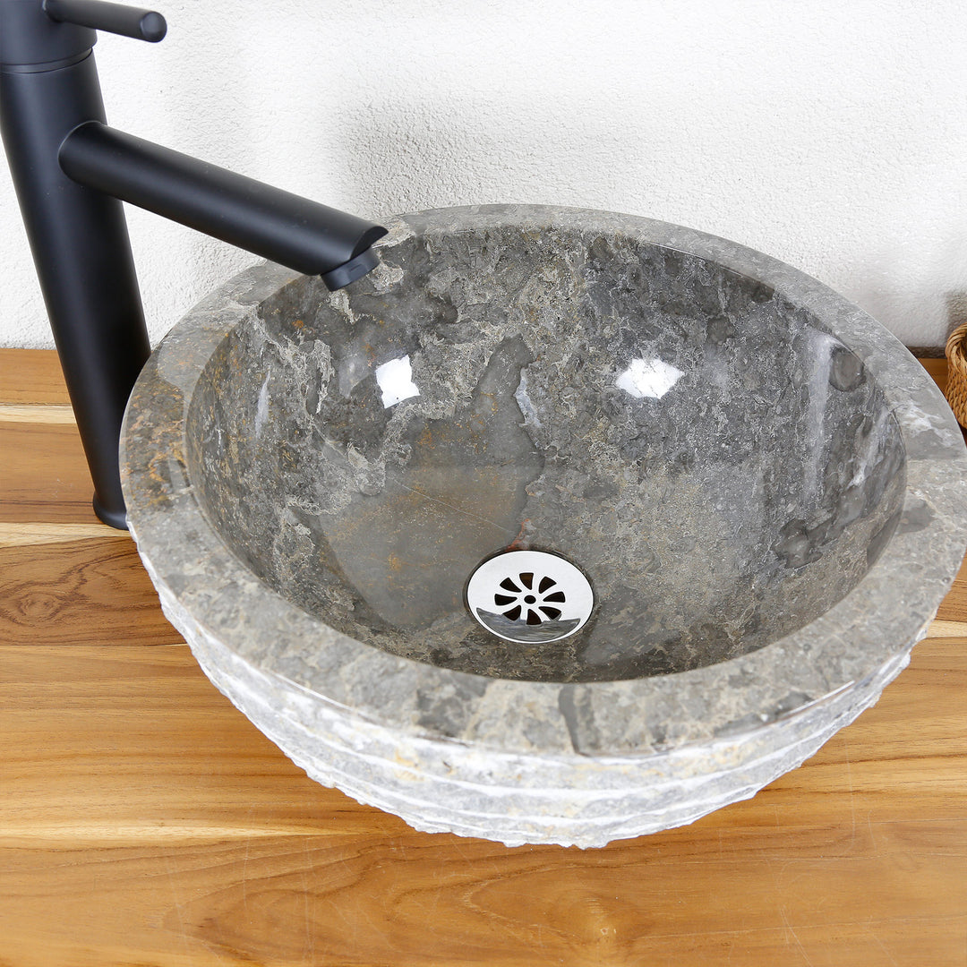 Ronde opzetwastafel van natuursteen met een gepolijste binnenkant en een gestructureerde buitenrand op een houten blad
