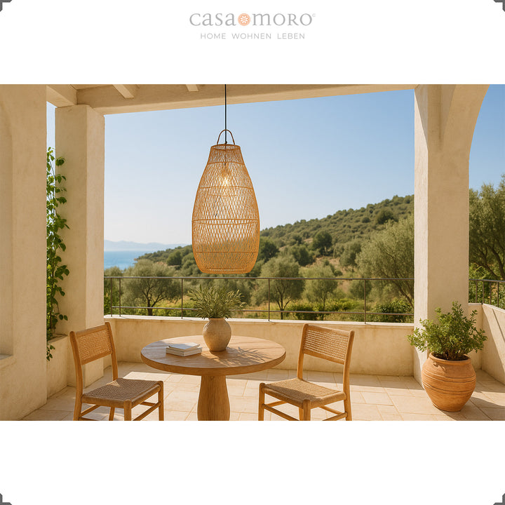 Große Rattanlampe über rundem Esstisch auf Terrasse mit Blick ins Grüne und mediterraner Atmosphäre