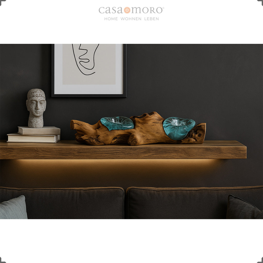 Länglicher Teelichthalter aus Glas und Wurzelholz auf einem Wandregal, sein warmes Licht ergänzt das stilvoll dunkle Wohnzimmerambiente.