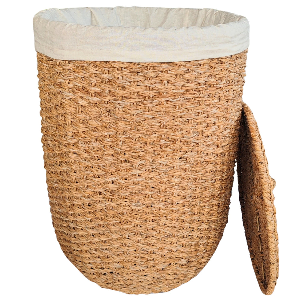 Open wasmand van naturelkleurig zeegras met een lichtgekleurde stoffen inzet en een aan de zijkant leunend deksel.