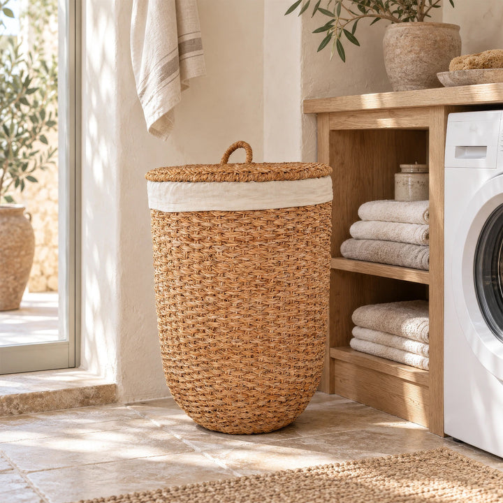 Een wasmand met deksel van natuurkleurig zeegras naast een handdoekenrek en een wasmachine in de wasruimte.