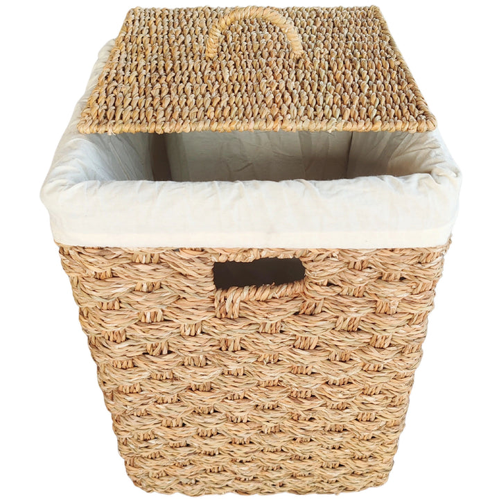 Vierkante wasmand van zeegras met een opstaande deksel, een lichtgekleurde stoffen inzet en een opening die als handvat dient.