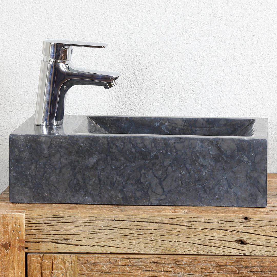 Vierkante opzetwastafel van marmer met donkere nerf op een houten console, gecombineerd met verchroomd beslag voor een lichte muur